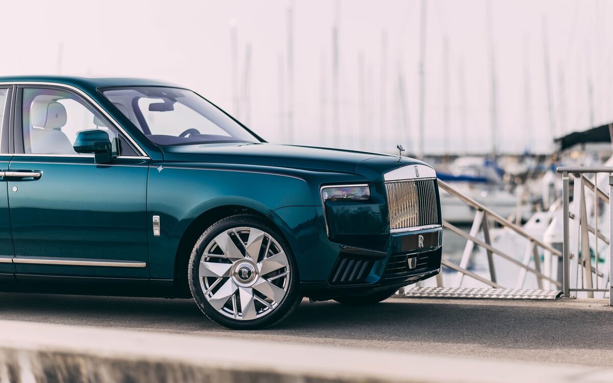Rolls-Royce Cullinan in teal parked by a harbour, front and side view with alloy wheel
