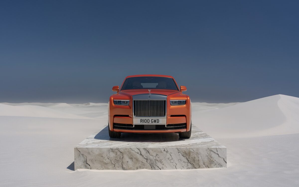 Rolls-Royce Phantom in orange seen from the front, standing on a marble plinth in a white desert