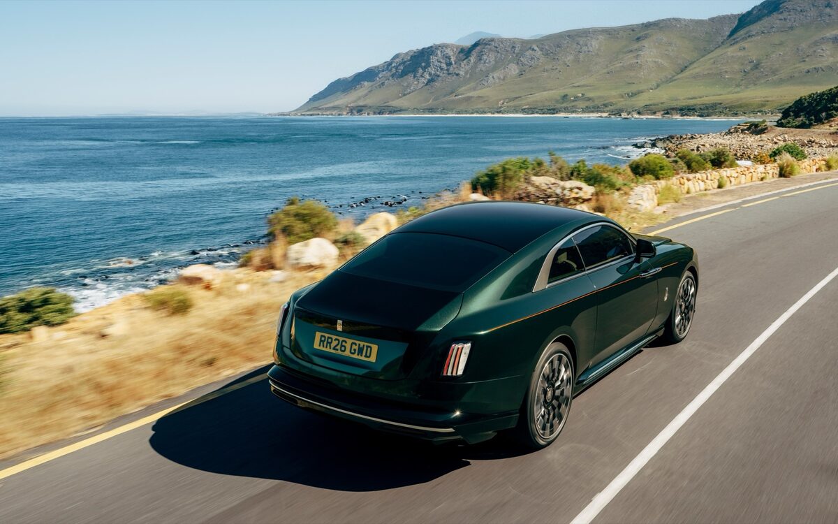 Rolls-Royce Spectre driving along a seaside road, rear three-quarter view
