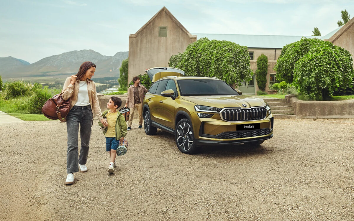 Skoda Kodiaq in Bronx Gold, front three-quarter view on a gravel drive with a family walking past
