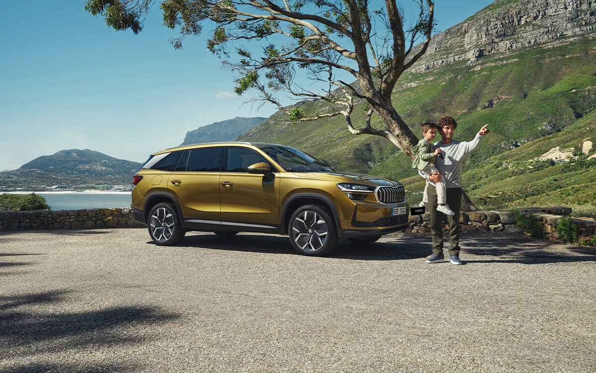 Skoda Kodiaq in Bronx Gold parked at a coastal viewpoint with a man and child beside it