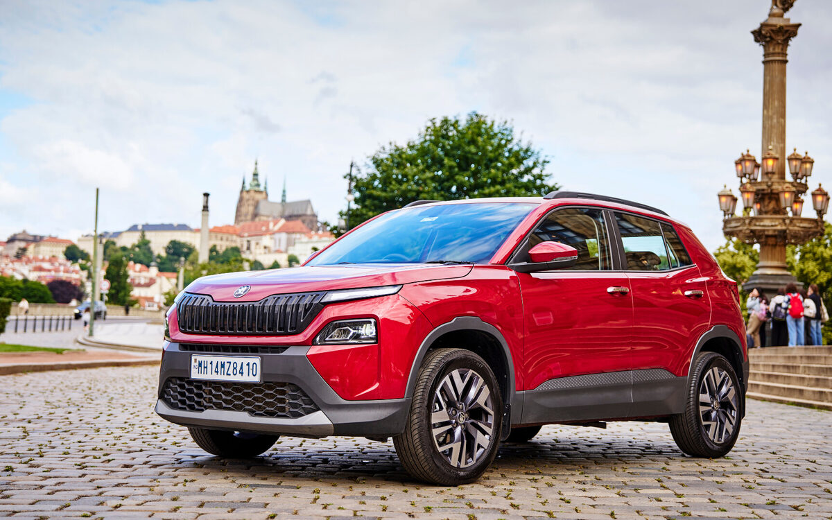 Skoda Kylaq in red, front three-quarter view parked on a cobbled square in front of a city skyline