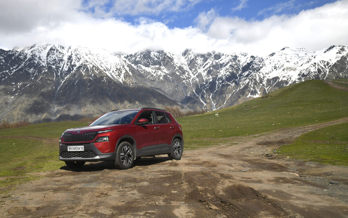 Skoda Kylaq in red parked on a dirt track with snow-capped mountains behind