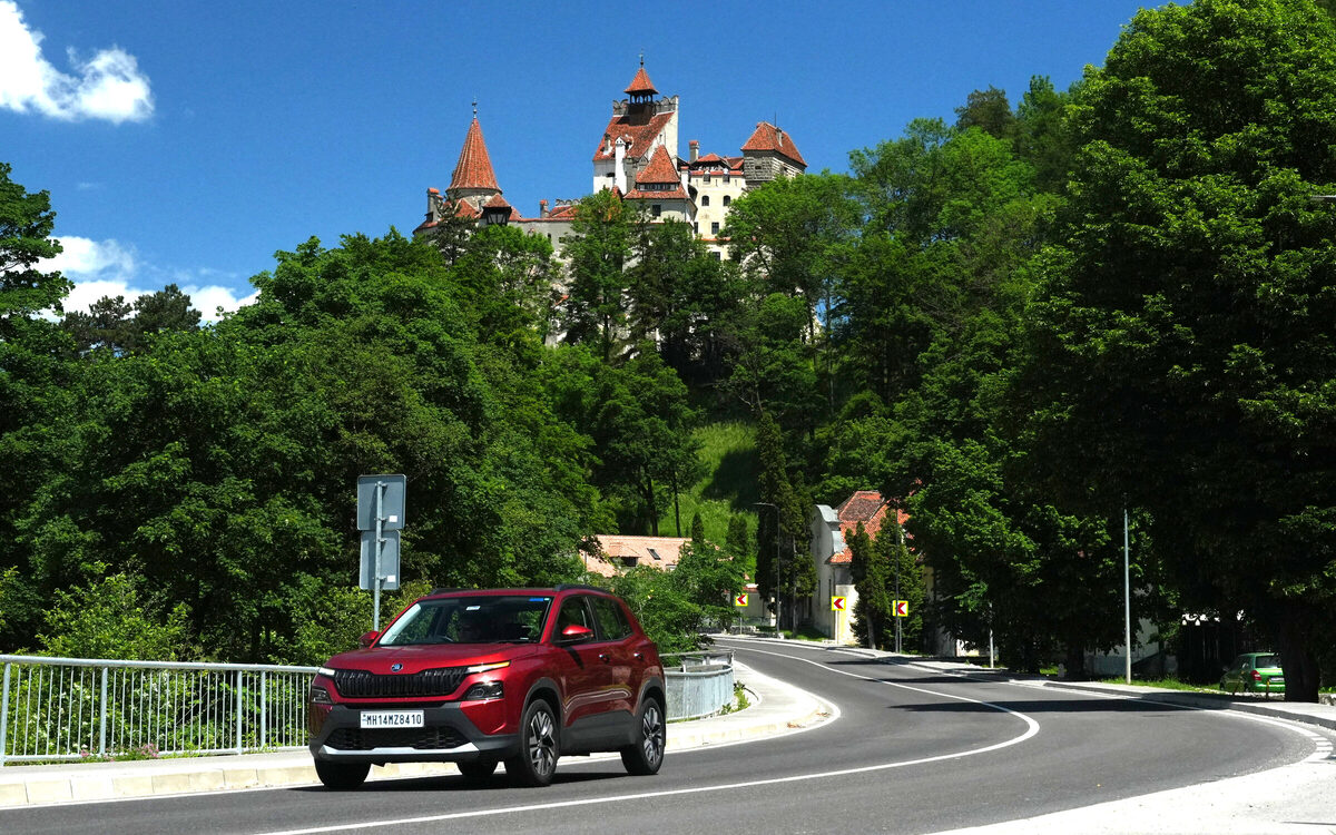Skoda Kylaq in red driving along a winding road with a hilltop castle in the background