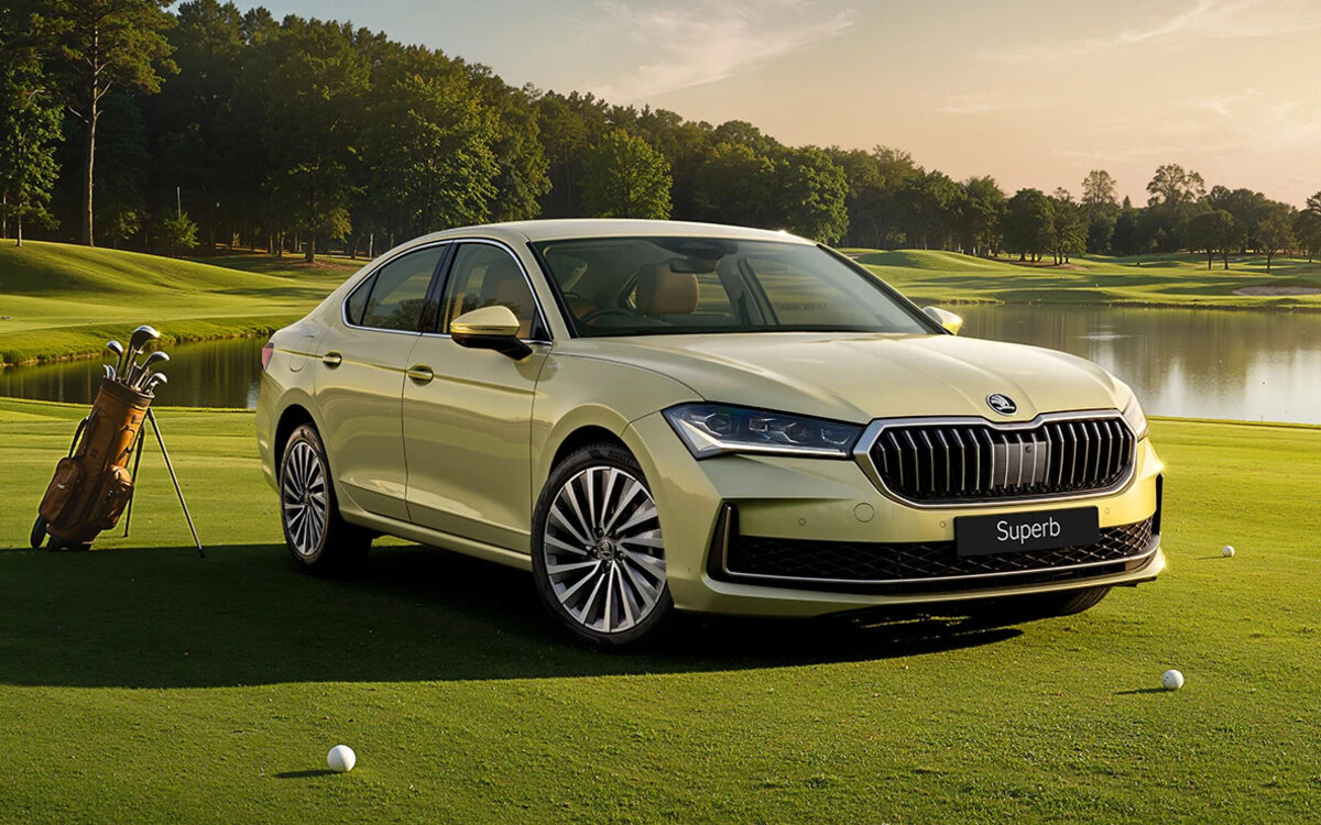 Skoda Superb in a pale gold-green, front three-quarter view parked on a golf course at sunset