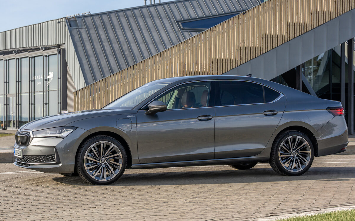 Grey Skoda Superb liftback seen from the front-left side, parked beside a modern building