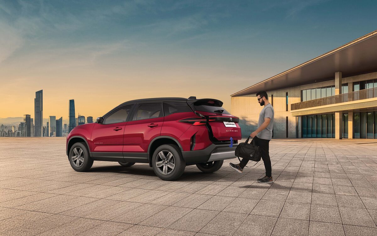 Tata Harrier in red, rear three-quarter view at sunset as a man opens the powered tailgate with a foot gesture