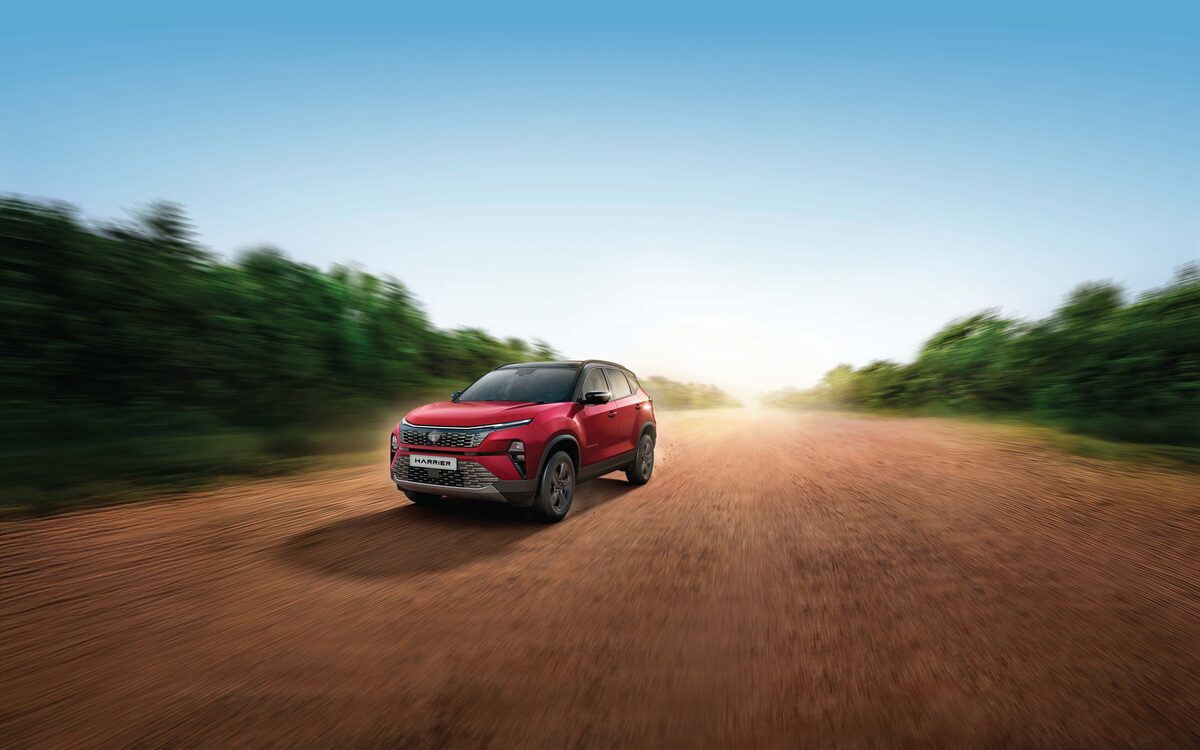 Tata Harrier in red driving towards the camera on a dirt road lined with trees