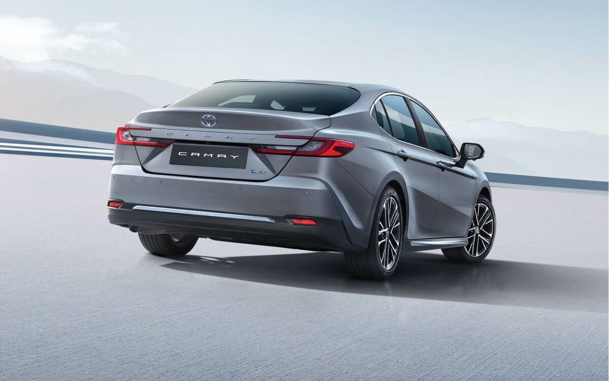 Grey Toyota Camry hybrid from the rear three-quarter, showing the connected tail lamps