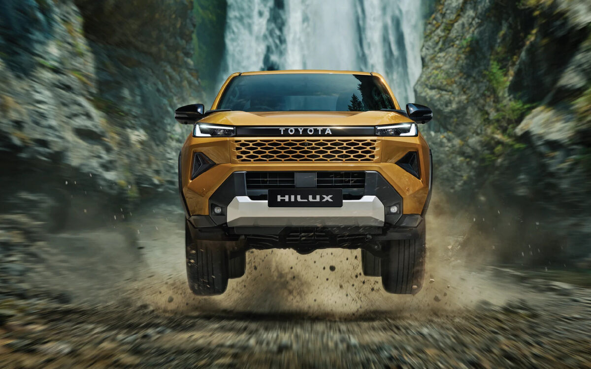 Toyota Hilux in Sulphur Metallic driving through a rocky stream below a waterfall, front view