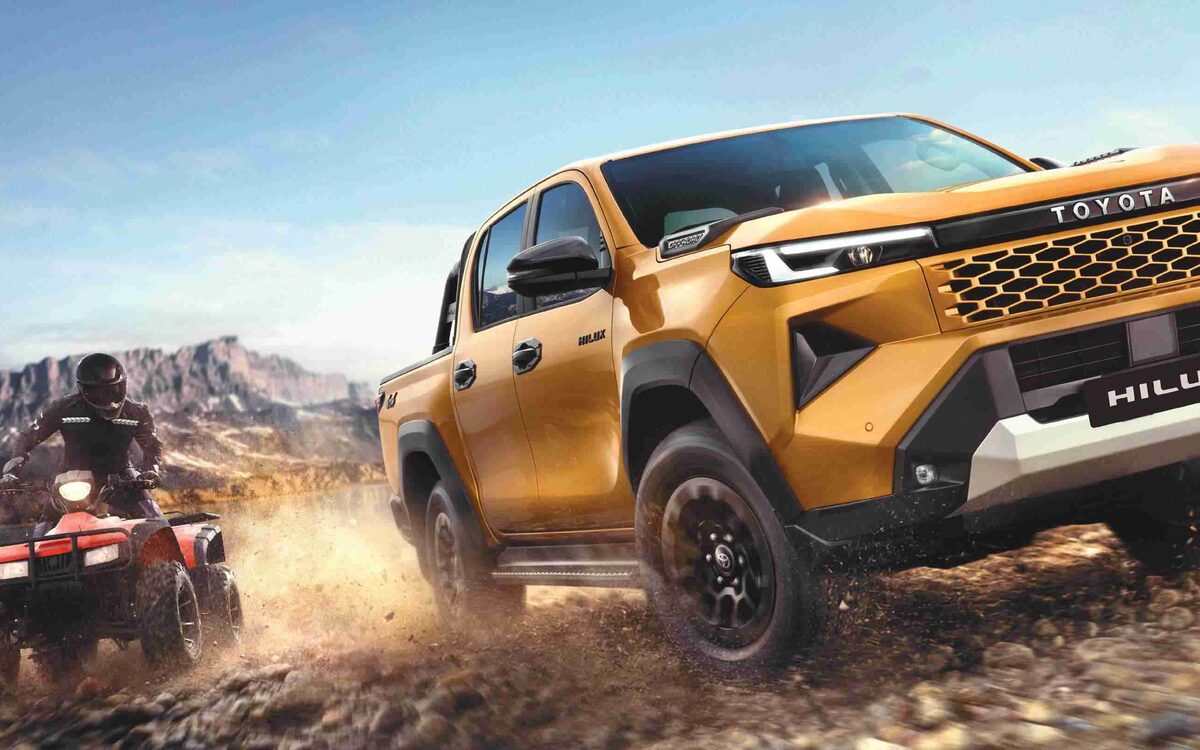 Toyota Hilux in Sulphur Metallic kicking up dust on a lakeside track with a quad bike behind