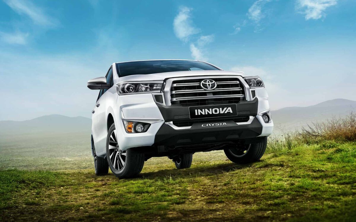 White Toyota Innova Crysta parked on a grassy hill, low front three-quarter view
