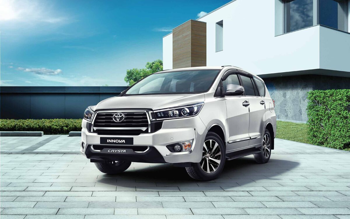 Pearl white Toyota Innova Crysta in front of a modern house, front three-quarter view