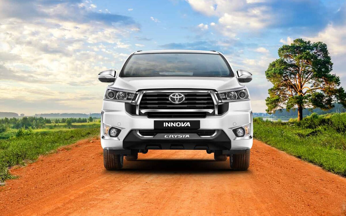 White Toyota Innova Crysta seen head-on on an orange dirt road with a tree beside it
