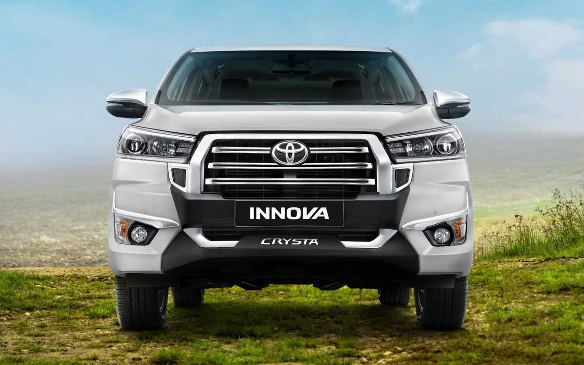 Head-on front view of a white Toyota Innova Crysta showing the grille and headlamps, on a grassy hill
