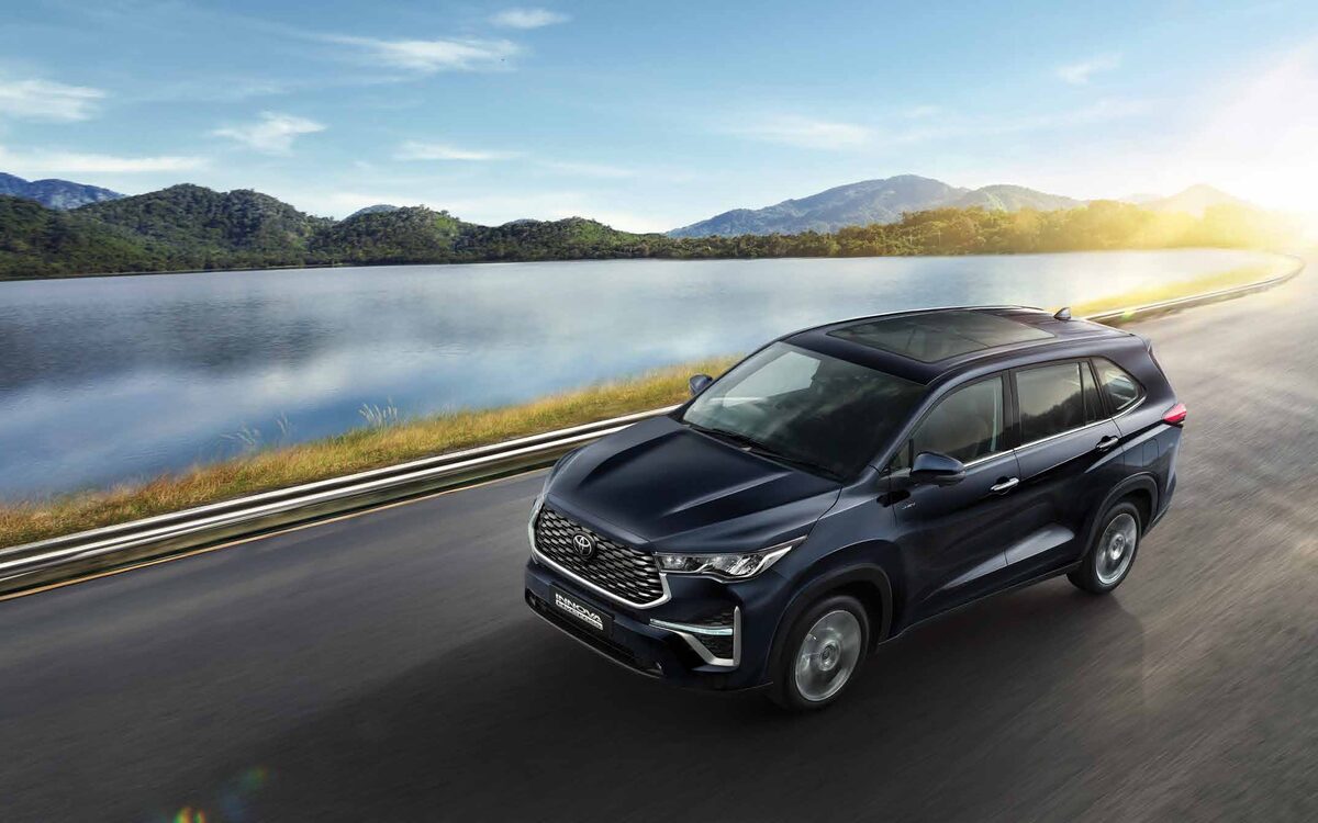 Toyota Innova HyCross in dark blue driving along a curved lakeside road with hills behind