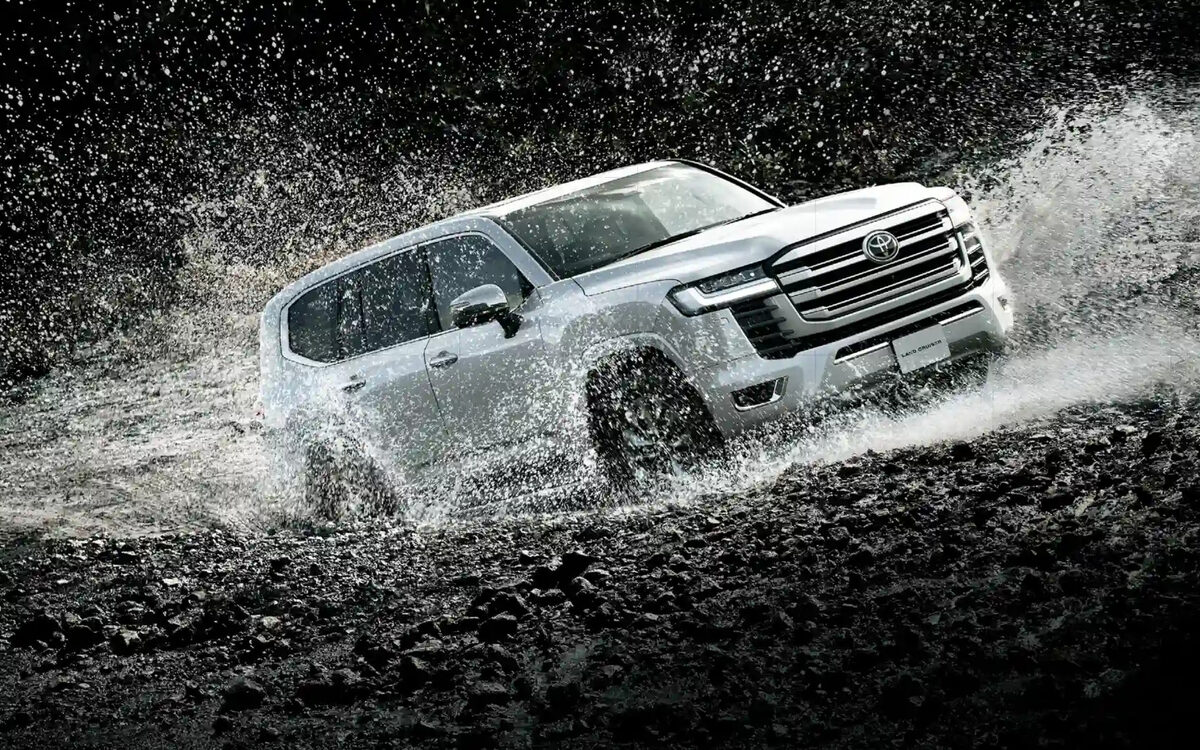 Toyota Land Cruiser in white driving fast through muddy water, front three-quarter view