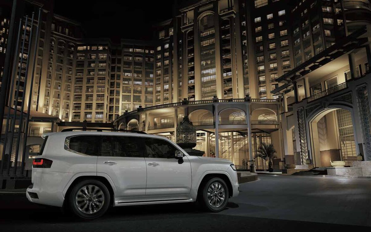 Toyota Land Cruiser in white parked outside a lit hotel at night, side view