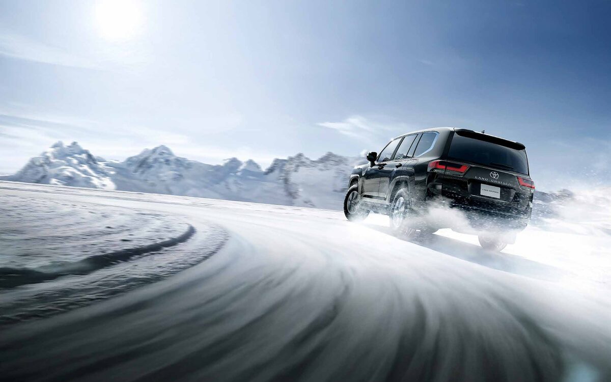 Black Toyota Land Cruiser driving on a snowy mountain road, rear three-quarter view