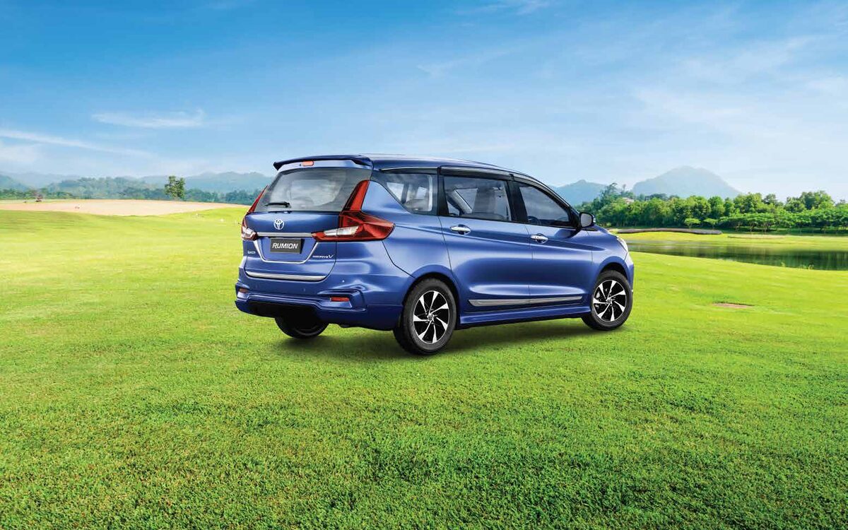 Blue Toyota Rumion on a lakeside lawn seen from the rear three-quarter