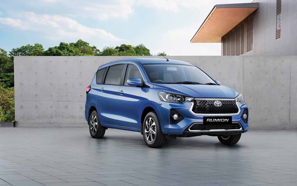 Blue Toyota Rumion parked in front of a concrete wall and modern building