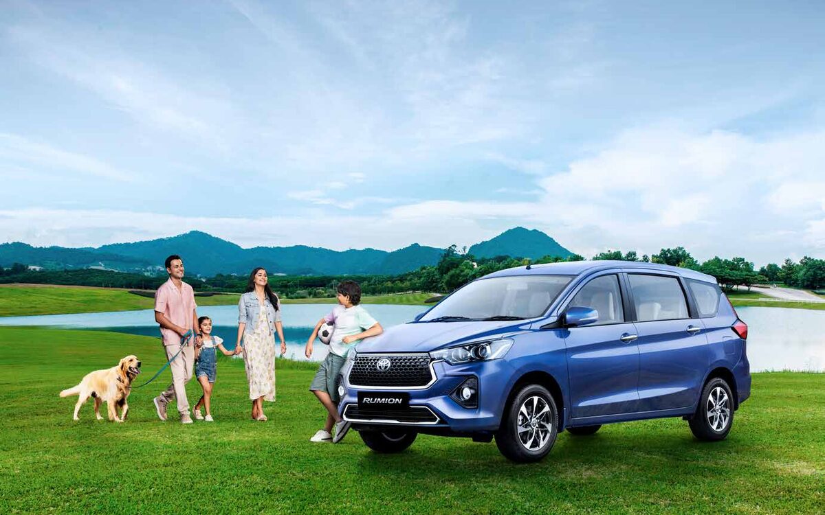 Blue Toyota Rumion on a lawn with a family and a dog standing beside it