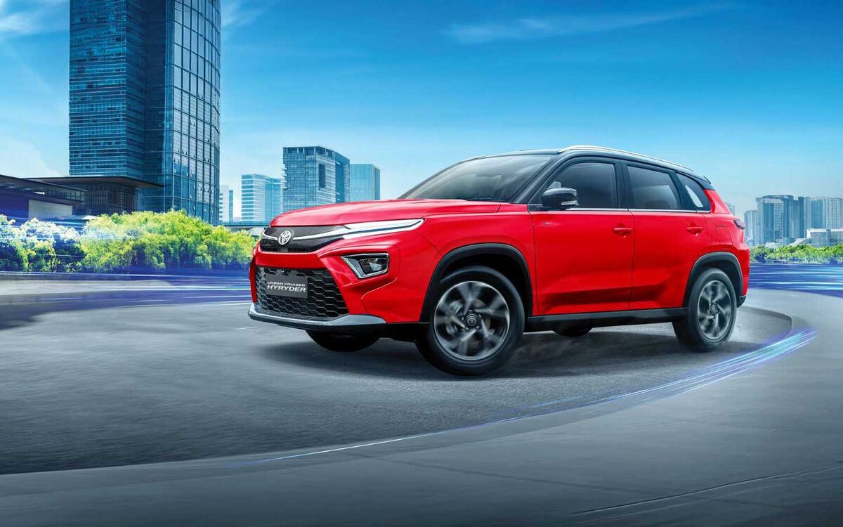 Toyota Urban Cruiser Hyryder in red taking a curve with tall glass buildings behind