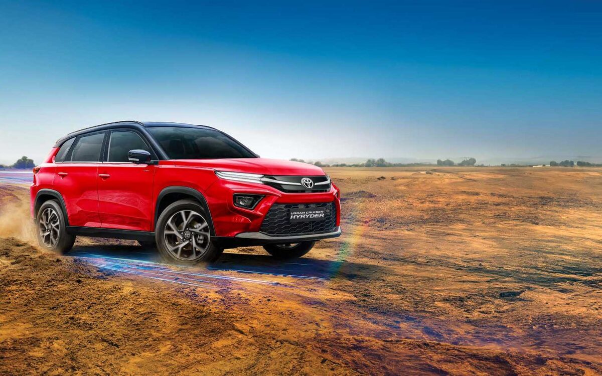 Toyota Urban Cruiser Hyryder in red kicking up dust on a dry open field
