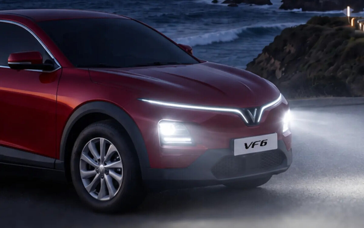 VinFast VF 6 in red, front end with the LED light bar and headlamps lit on a coastal road at night