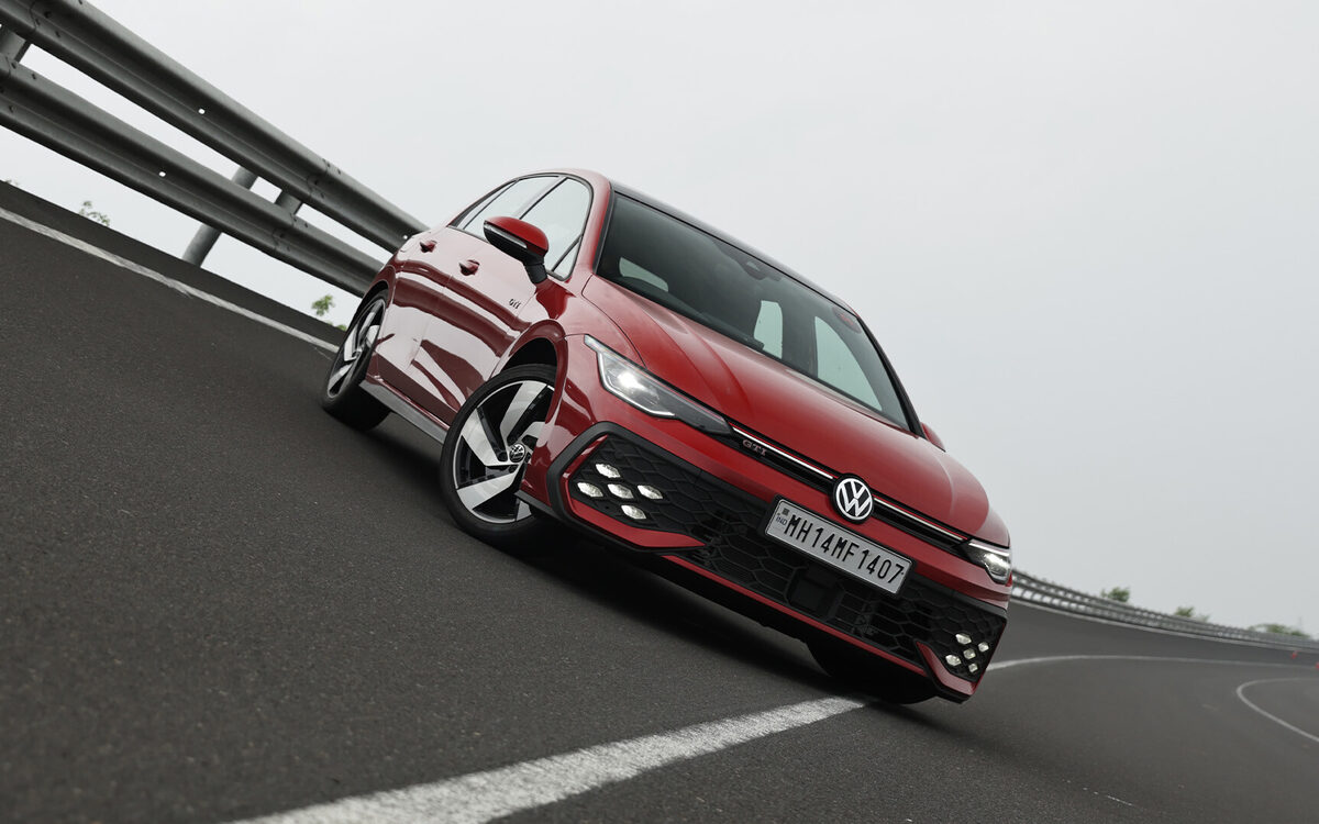 Red Golf GTI leaning through a banked bend on a test track, seen from the front