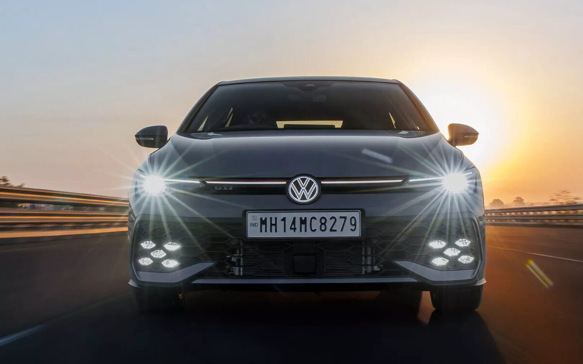 Grey Golf GTI driving head-on toward the sunset with LED headlamps and fog lamps lit