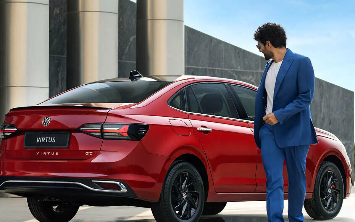 Virtus in red seen from the rear quarter with the tail lamp and boot lid, a man walking beside it
